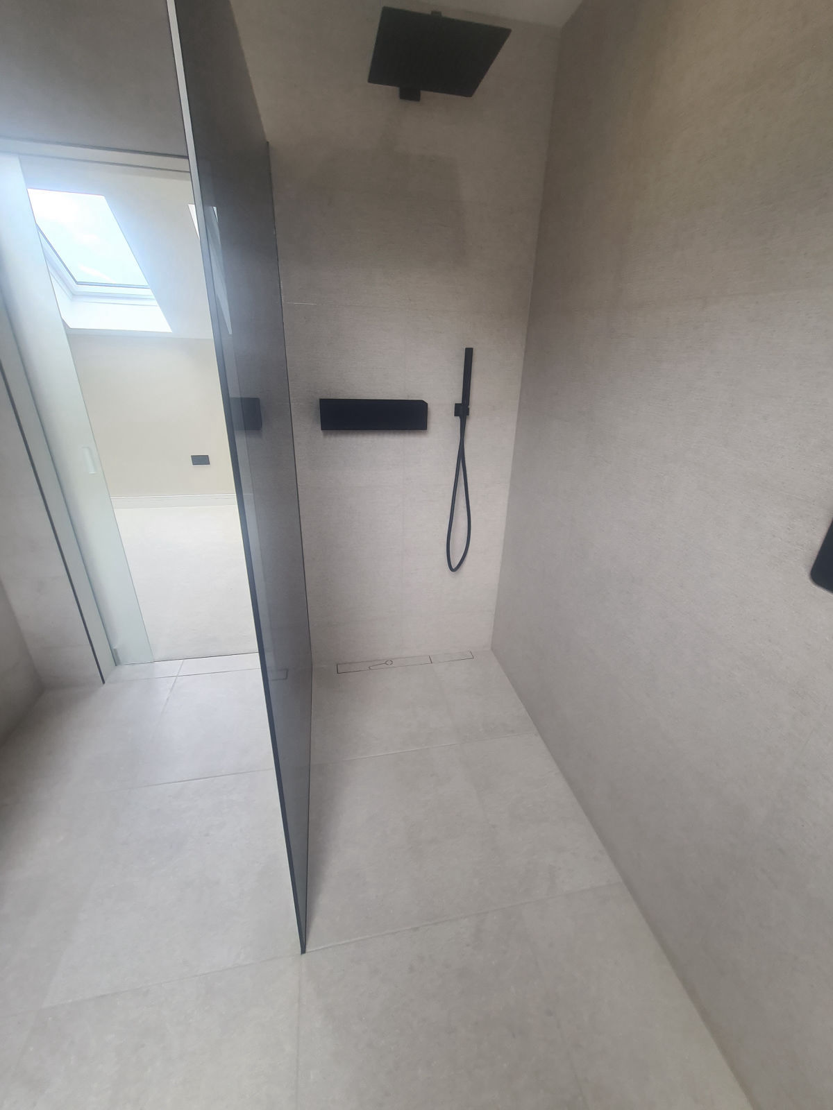 A level-access wet room in stone-effect porcelain with a linear drain and black fittings
