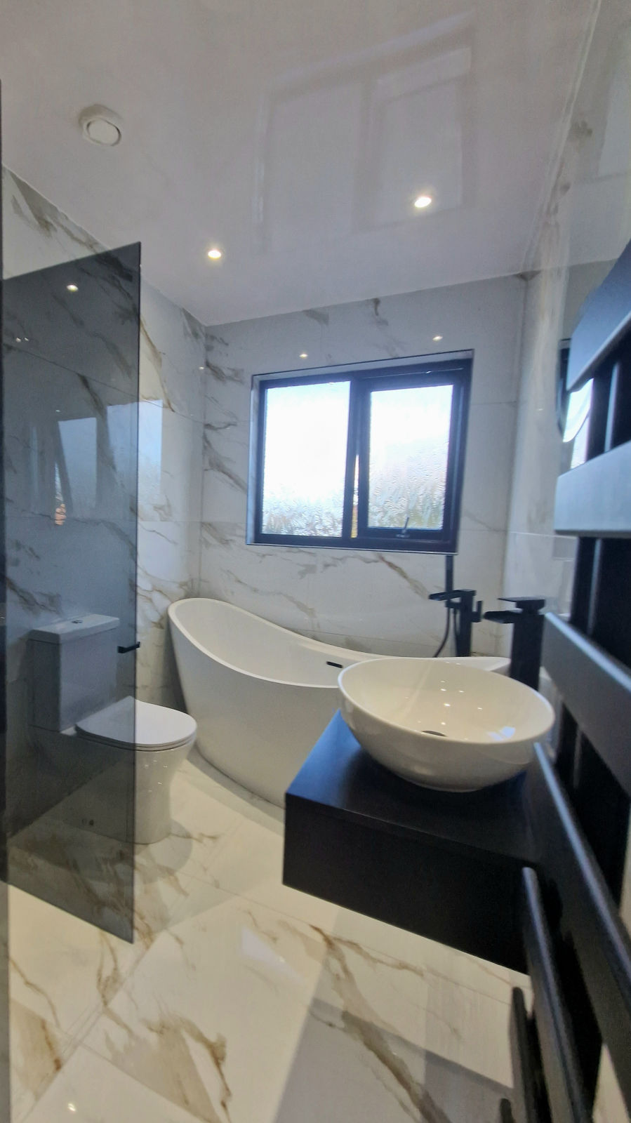 A freestanding slipper bath under a window, with a vessel basin on a black shelf