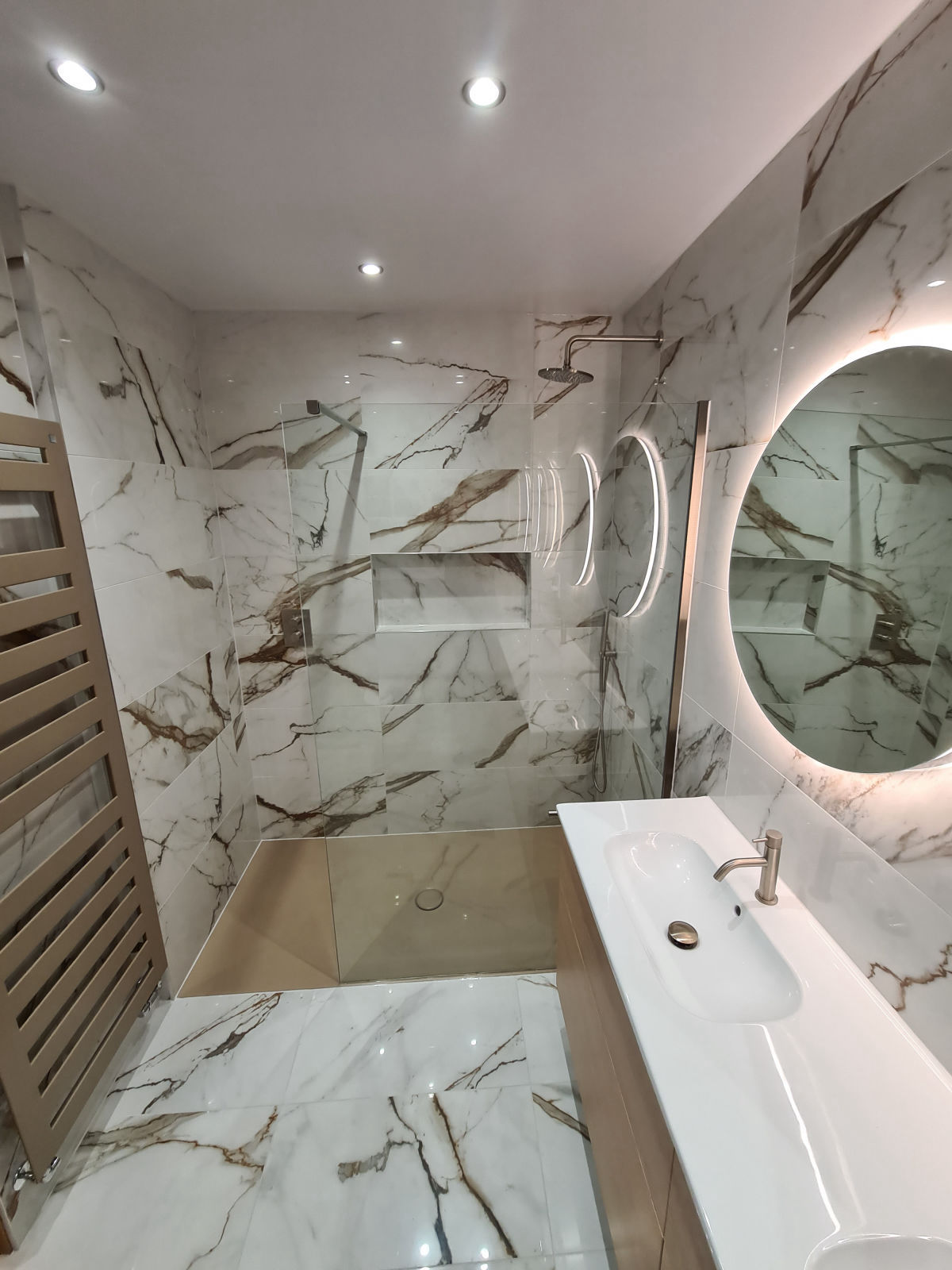 A marble en suite with a walk-in shower, a recessed niche and a round backlit mirror